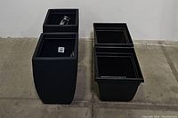 Photo showing two large black curved square planters on the left, new with tags inside, and two smaller used black square planters on the right.