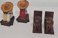 Pair of carved wooden Mexican folk art figures sitting with wide-brimmed hats on wooden bases, and pair of carved wooden elephant bookends showing back view on wooden L-shaped bases.
