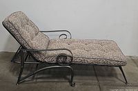Side view of the metal chaise lounge showing the frame, curved armrest detail, and floral cushion.