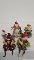 All five Christmas figurines shown together including two fairy elves seated, three Santa Claus figures, and one small snowman figurine.