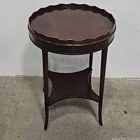 Full front photo of round wooden espresso end table showing scalloped top and curved display shelf.
