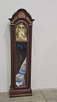 Full view of tall grandfather clock showing the wooden case with glass front door and bonnet top.
