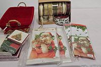 Holiday decor lot showing the red lined basket, two kitchen towels with Santa Claus designs, and assorted holiday paper napkins with Christmas tree design.