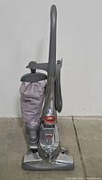 Full front view of the vintage Kirby upright vacuum cleaner standing on floor, showing the handle, dust bag, and base.