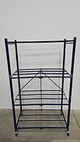 Front view of blue metal storage rack with four wire grid shelves and caster wheels.