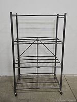 Front view of silver 4-shelf foldable metal storage rack with wire mesh shelves and caster wheels against a plain wall.
