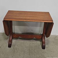 Wooden mid century expandable pedestal table folded with drop leaves down.