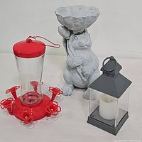All three items together on table: concrete animal planter sculpture, red hummingbird feeder, gray plastic flameless lantern