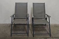 Front view of pair of dark gray metal outdoor folding patio lawn chairs showing mesh fabric seats and backs with armrests.