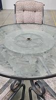 Close-up of round glass tabletop with etched leaf design and wrought iron frame underneath