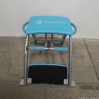 Front view of Pilates Pro Chair showing padded turquoise seat, metal frame, and footrest