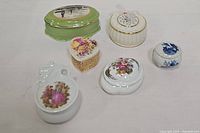Overview of six assorted porcelain lidded trinket boxes showing varied shapes and painted designs