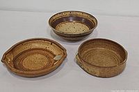 Three stoneware pieces: two round bowls and one oval platter with handles, all speckled brown and beige pottery.