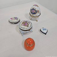 Overall view of five assorted trinket boxes on white surface, porcelain, lucite and metal accents