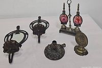 Overview of the lot including two metal wall sconces with oval mirrors, the metal bookend with pink glass bottle decorations, and the brass candlestick holder.