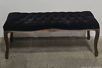 Front view of the black velvet tufted Victorian style bench showing wooden legs and apron with carved details.