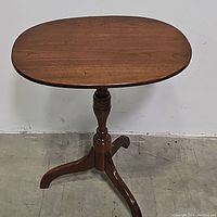 Front view of a vintage wooden oval side table showing the oval tabletop and turned pedestal base with tripod legs.