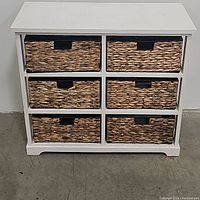 Front view of the wicker basket storage chest with all six baskets inserted neatly in place showing the distressed white wooden frame and the basket handles.