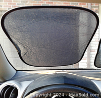 View through dark mesh sun shade clipped inside car window, showing how it fits the window and blocks sunlight.