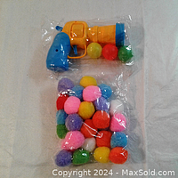 Close-up photo of the plastic pop shooter toy gun with fuzz balls in packaging.