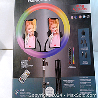 Packaging showing the front of the product box detailing features including dual phone cradles, 15 RGB colors, wireless remote control, USB powered, compact and portable design, and adjustable 63-inch light stand.