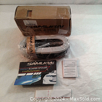 Photo of the coiled flexible black rubber front bumper spoiler with 3M adhesive tape, accompanied by printed instructions and original cardboard packaging.