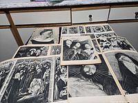 Overview of numerous black-and-white art plates spread on countertop, visible Primitifs Francais cover and various religious scenes