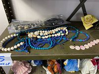 Photo of multiple strands of costume jewelry in blue, white, and pink colors on shelf including beads and bracelets.