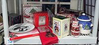 Shelf display of multiple Christmas holiday items including plates, tins, jars, and textile.