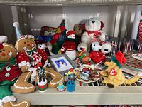 Shelf with Christmas plush toys including white polar bear, yellow Ty dog in elf hat, gingerbread men plush dolls, and holiday pins with books and CDs in background.