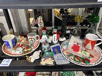 Photo of assorted Christmas mugs, trays, snowman figurines, and various holiday ornaments arranged on a shelf.