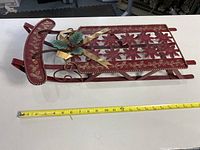 Side view of a red wooden sled with metal runners, poinsettia cutouts, and gold leaf detail with ribbon and faux holly accent