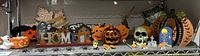 Full view of assorted fall and Halloween decorations arranged on a shelf with pumpkin, ghost, skull, web, and house motifs