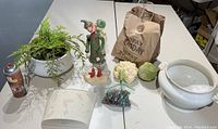 Overview of lot showing floral arrangement, vintage figures, fake vegetables, letter holder, and bag of decorative items.