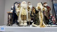 Group of seven Santa Claus and winter figures in various colors and size on shelf; shows diverse styles and details