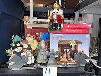 Photo showing grouped Christmas decorations including a large wooden nutcracker figure, porcelain nativity sets in box, and snowman coaster set.