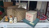 Overview of lot on shelf showing boxed and unboxed items including figurines, salt and pepper shakers, candy dish, and trays