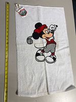 White golf towel with Mickey Mouse in golf outfit and Disney tag
