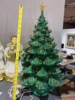 Photo showing the large green ceramic Christmas tree with multicolored bulb lights and star topper, measuring about 13 inches tall, with the choir angels visible in background.