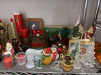 Shelf display of assorted vintage Christmas decorations including glass Christmas tree ornaments, Santa figurines, wreaths, candle holders, and electric window candles.