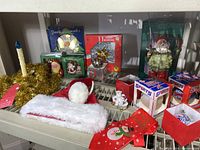 Display shelf with various Christmas ornaments and holiday accessories including Santa hat, holiday tie, tinsel candle holder, and boxed glass ball ornaments.