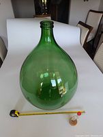 Front view of large green glass demijohn with measuring tape for scale showing its size.