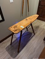 Side view of the antique wooden ironing board showing wood grain and folding legs.