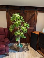 Full view of artificial Japanese Maple tree placed indoors near a red fabric armchair and wooden sliding barn door, showing the overall height and realistic leaves.