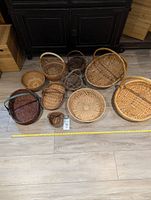 View of 11 assorted woven baskets in various sizes and shapes, shown on floor with tape measure for scale.