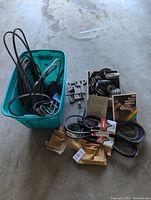 Photo of green tote with assorted belts including V-belts and toothed belts inside. Leather tool belt visible on top with metal pulleys and a book next to tote.