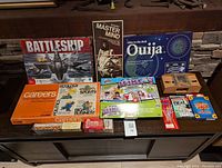 Overview of the assorted board games lot showing Battleship, Super Master Mind, Ouija, Careers, Slime Laboratory, and vintage electronic game.
