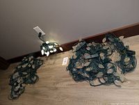 Several tangled strands of white LED Christmas lights on green wiring, lit up partially from one plug.