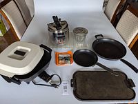 Overview of lot showing all items on table including Lagostina pressure cooker, electric grill pan, 2 non-stick pans, dessert mold, cast iron griddle.