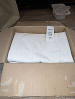 Curtains folded neatly inside a cardboard box, showing white linen fabric.